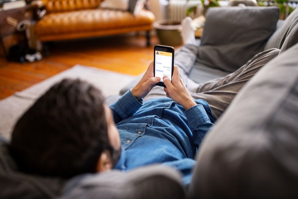 man using smartphone in sofa man chatting with friend on mobile phone messaging app
