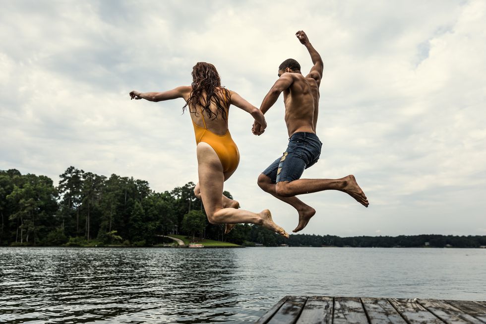 young couple jumping off dock into lake